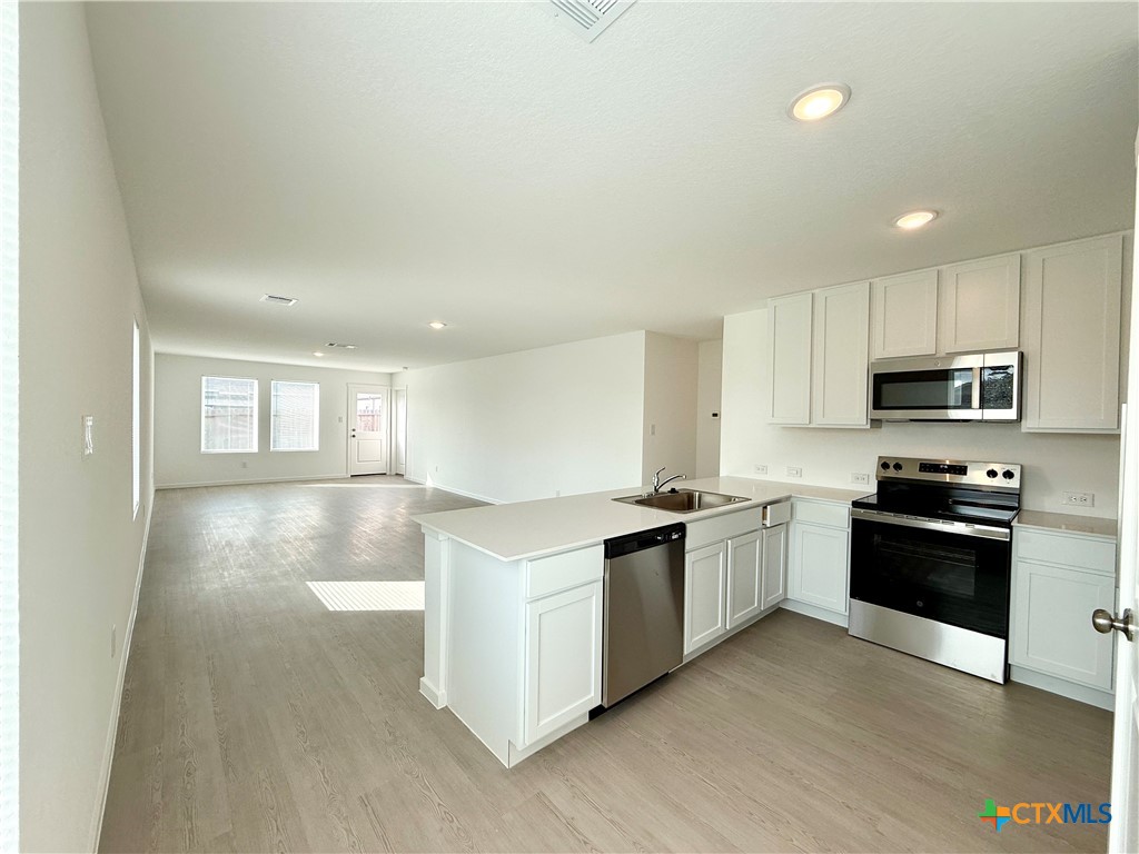 311 Moscato Road New Braunfels, TX 78130 - Photo 3 of 38 a kitchen with stainless steel appliances granite countertop a stove top oven a sink dishwasher and a refrigerator with wooden floor