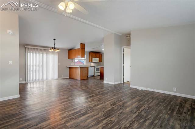 20150 Enoch Road Colorado Springs, CO 80928 - Photo 12 of 50 Unfurnished living room with vaulted ceiling, dark wood-type flooring, baseboards, ceiling fan, and a sink