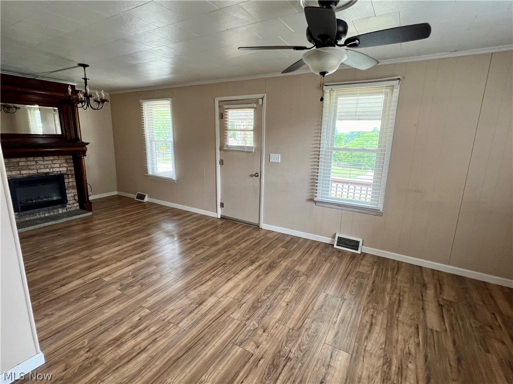 Unfurnished living room featuring ceiling fan, crown molding, a brick fireplace, and wood-type flooring