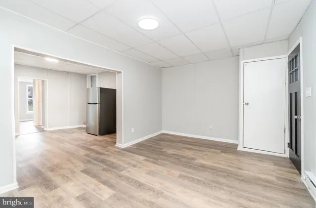a view of an empty room with wooden floor and kitchen view