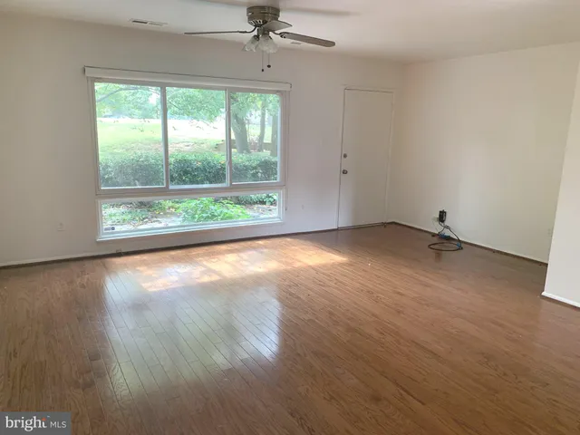an empty room with wooden floor fan and windows