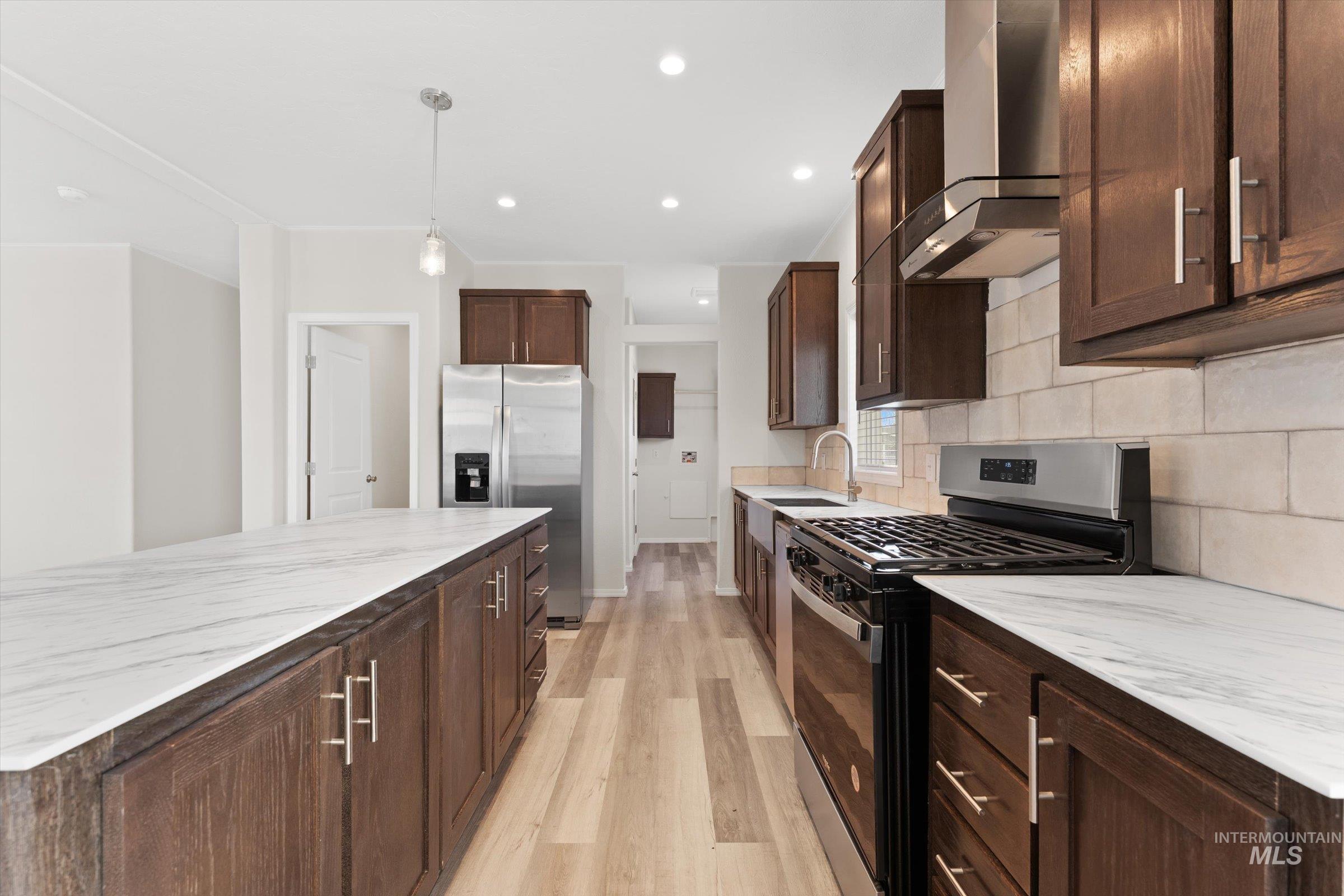 421 South Curtis Road, Unit 34 34 Boise, ID 83705 - Photo 6 of 22 Kitchen featuring appliances with stainless steel finishes, dark brown cabinets, wall chimney exhaust hood, hanging light fixtures, and light wood-type flooring