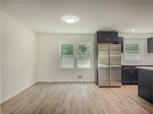 an empty room with wooden floor kitchen view and windows