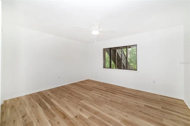 an empty room with wooden floor ceiling fan and windows