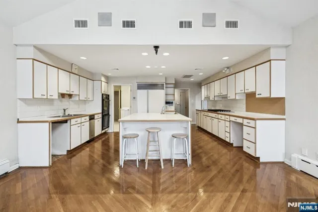 a kitchen with stainless steel appliances kitchen island granite countertop a stove a sink a refrigerator and white cabinets with wooden floor