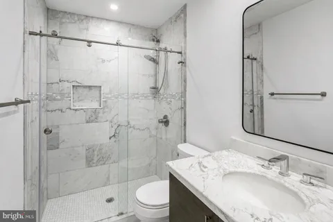 a bathroom with a granite countertop shower sink vanity mirror and toilet