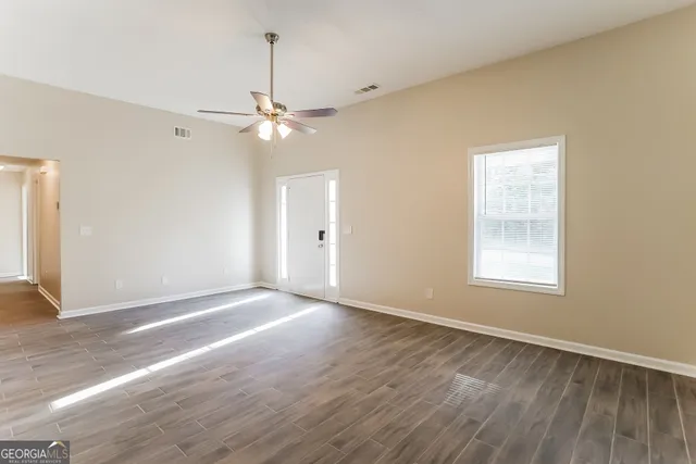 an empty room with wooden floor chandelier fan and windows