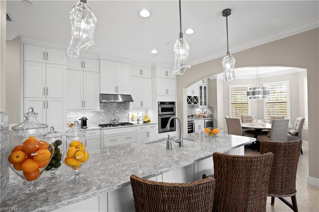 16391 Viansa Way, Unit 101 Naples, FL 34110 - Photo 15 of 48 a kitchen with stainless steel appliances granite countertop a stove a kitchen island a dining table and chairs