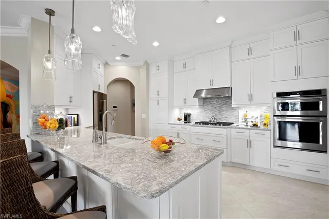 a large kitchen with granite countertop a stove a sink a dining table and chairs with white cabinets