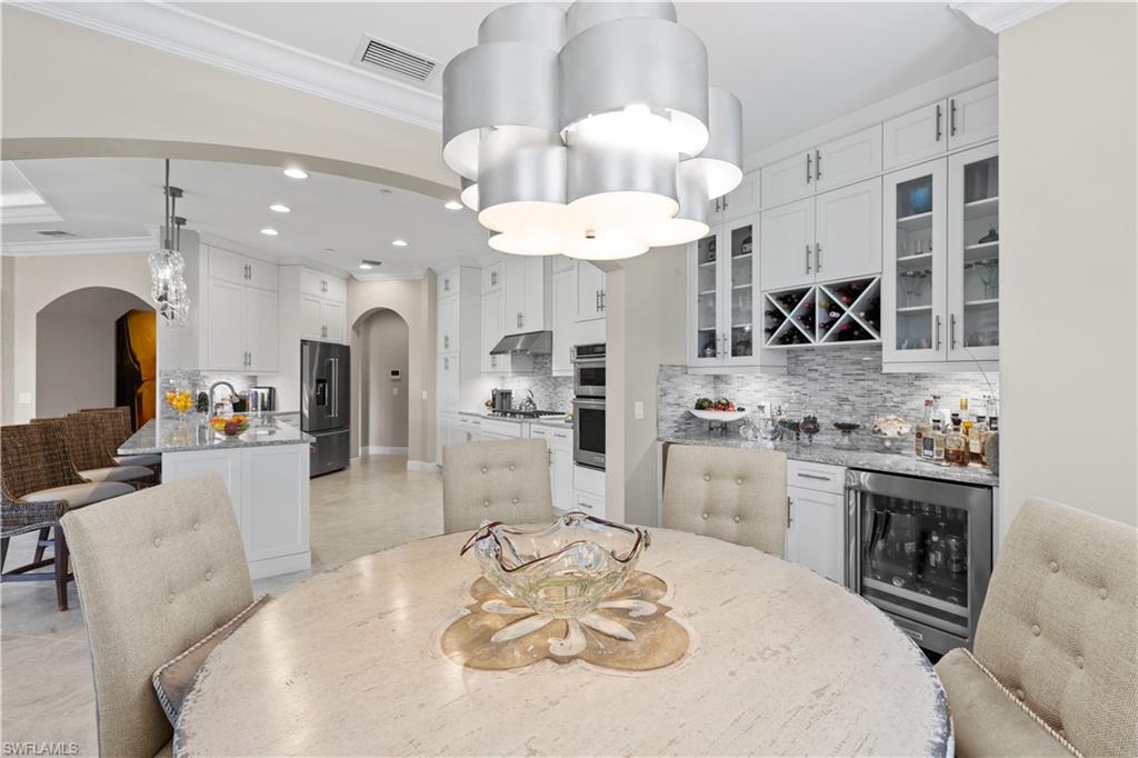 16391 Viansa Way, Unit 101 Naples, FL 34110 - Photo 19 of 48 a large kitchen with granite countertop a stove a sink a dining table and chairs with white cabinets