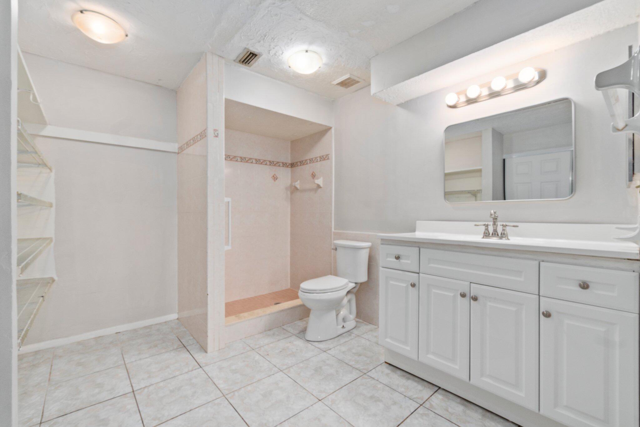 6012 Indrio Road, Unit E2 Fort Pierce, FL 34951 - Photo 15 of 25 a spacious bathroom with a toilet a sink a mirror and a shower