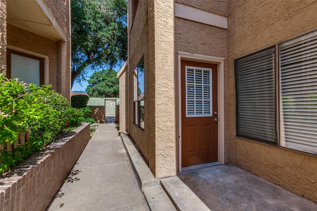 5550 Spring Valley Road, Unit C16 Dallas, TX 75254 - Photo 8 of 22 Brown entry door with a white louvered window, textured stucco exterior, and concrete walkway