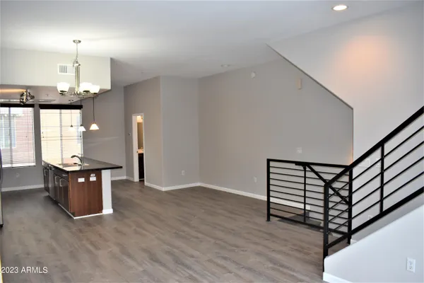 a view of an empty room with wooden floor stairs and a way to kitchen