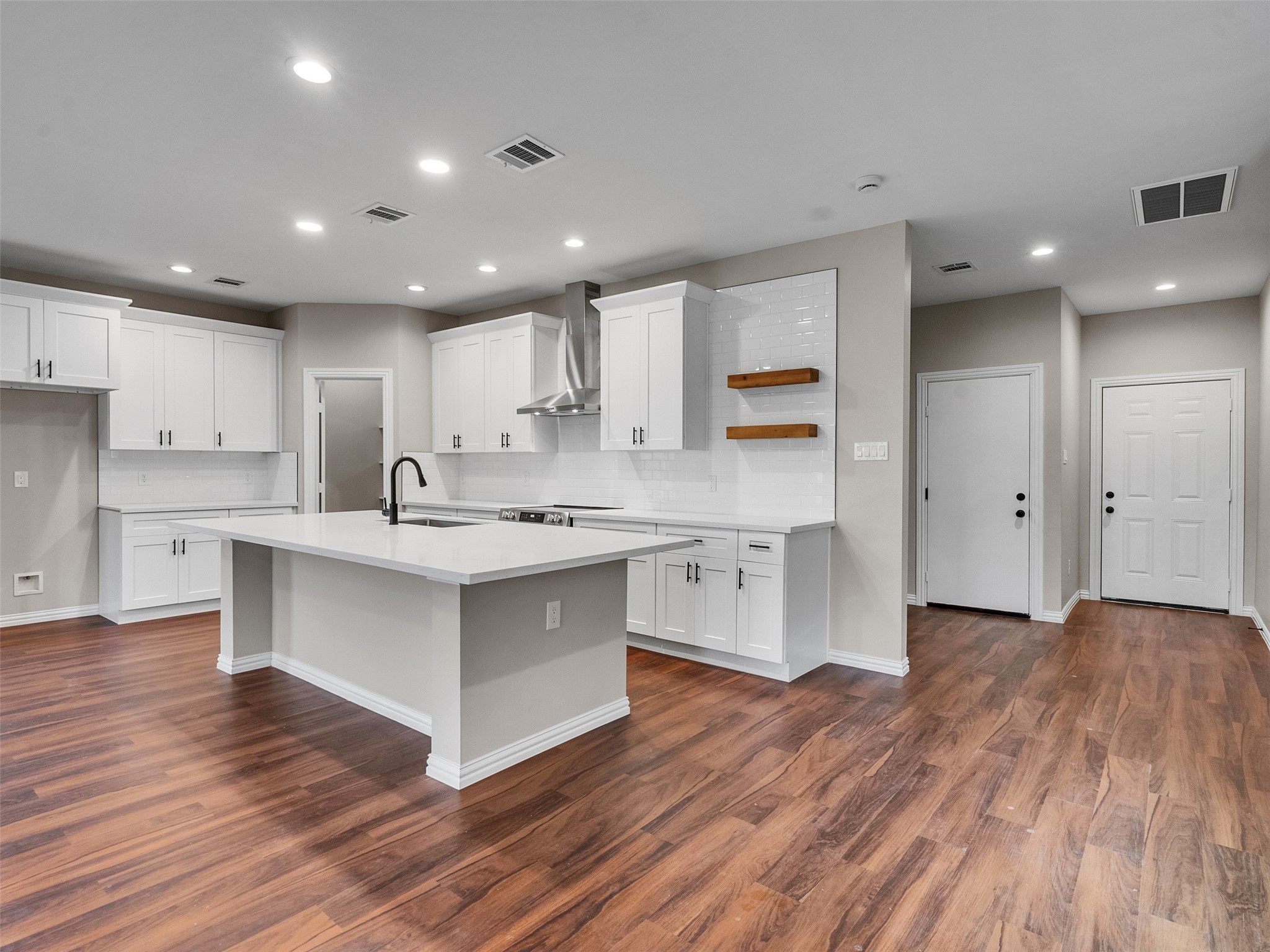 a large white kitchen with a center island wooden floor stainless steel appliances and cabinets
