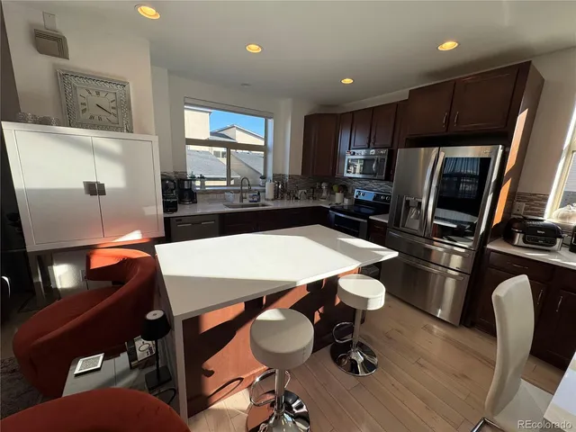 a kitchen with stainless steel appliances granite countertop a refrigerator a stove a sink a dining table and chairs with wooden floor