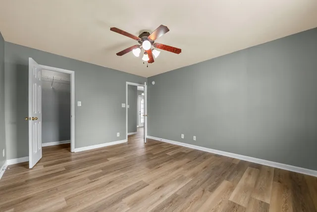a view of an empty room with wooden floor and a ceiling fan