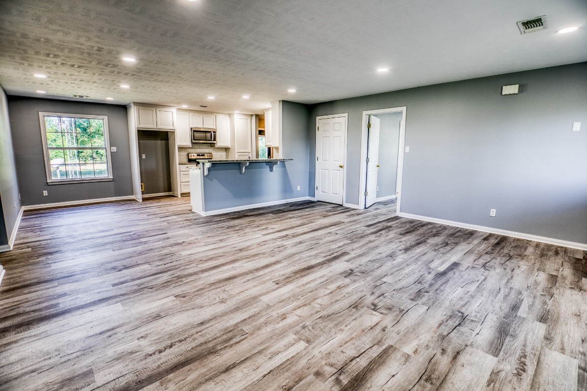an empty room with wooden floor kitchen view and windows