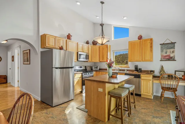 a kitchen with stainless steel appliances granite countertop a refrigerator a sink a stove and a dining table with wooden floor