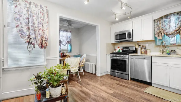 a kitchen with stainless steel appliances a white stove top oven a sink a dining table and chairs with wooden floor