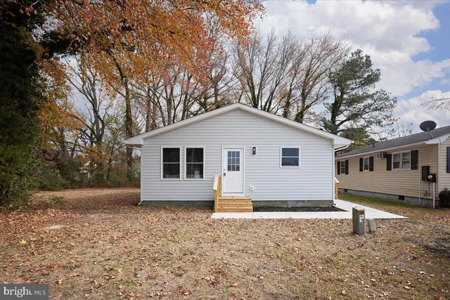 a view of a white house next to a yard with a tree
