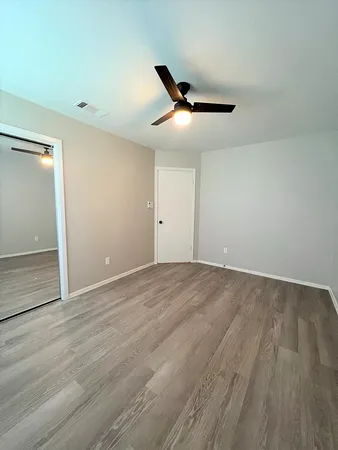 an empty room with wooden floor fan and windows