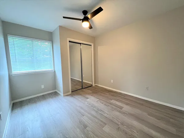 an empty room with wooden floor ceiling fan and windows
