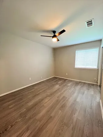 an empty room with wooden floor ceiling fan and windows
