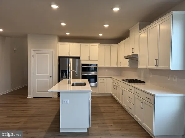 a large kitchen with stainless steel appliances granite countertop a stove a sink dishwasher a refrigerator and white cabinets with wooden floor