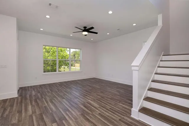 an empty room with wooden floor fan and windows