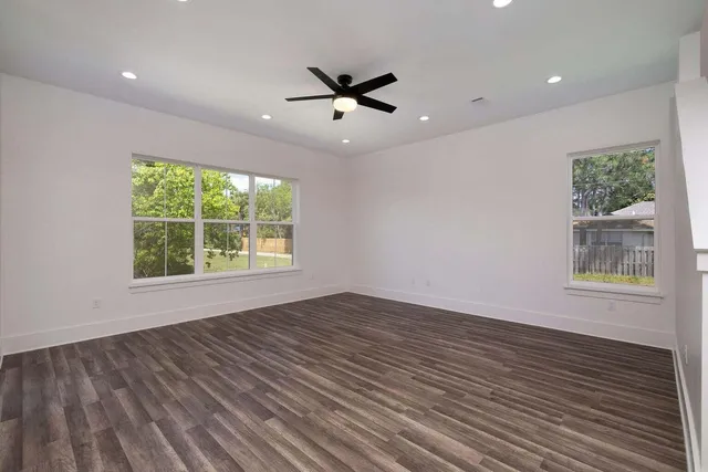 an empty room with wooden floor a ceiling fan and windows