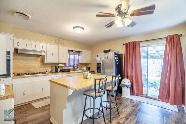 a kitchen with stainless steel appliances granite countertop a stove a refrigerator a sink a dining table and chairs with wooden floor