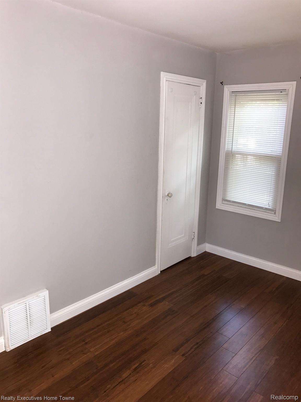 2427 Cambridge Road Berkley, MI 48072 - Photo 13 of 17 Room featuring warm wood-finish flooring, light gray walls, white trim, a white paneled door, and a window with white blinds