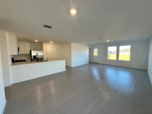 a view of an empty room with kitchen and window