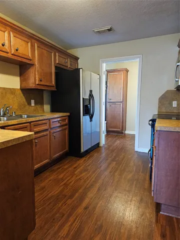 a kitchen with stainless steel appliances granite countertop a refrigerator a sink dishwasher and wooden cabinets with wooden floor