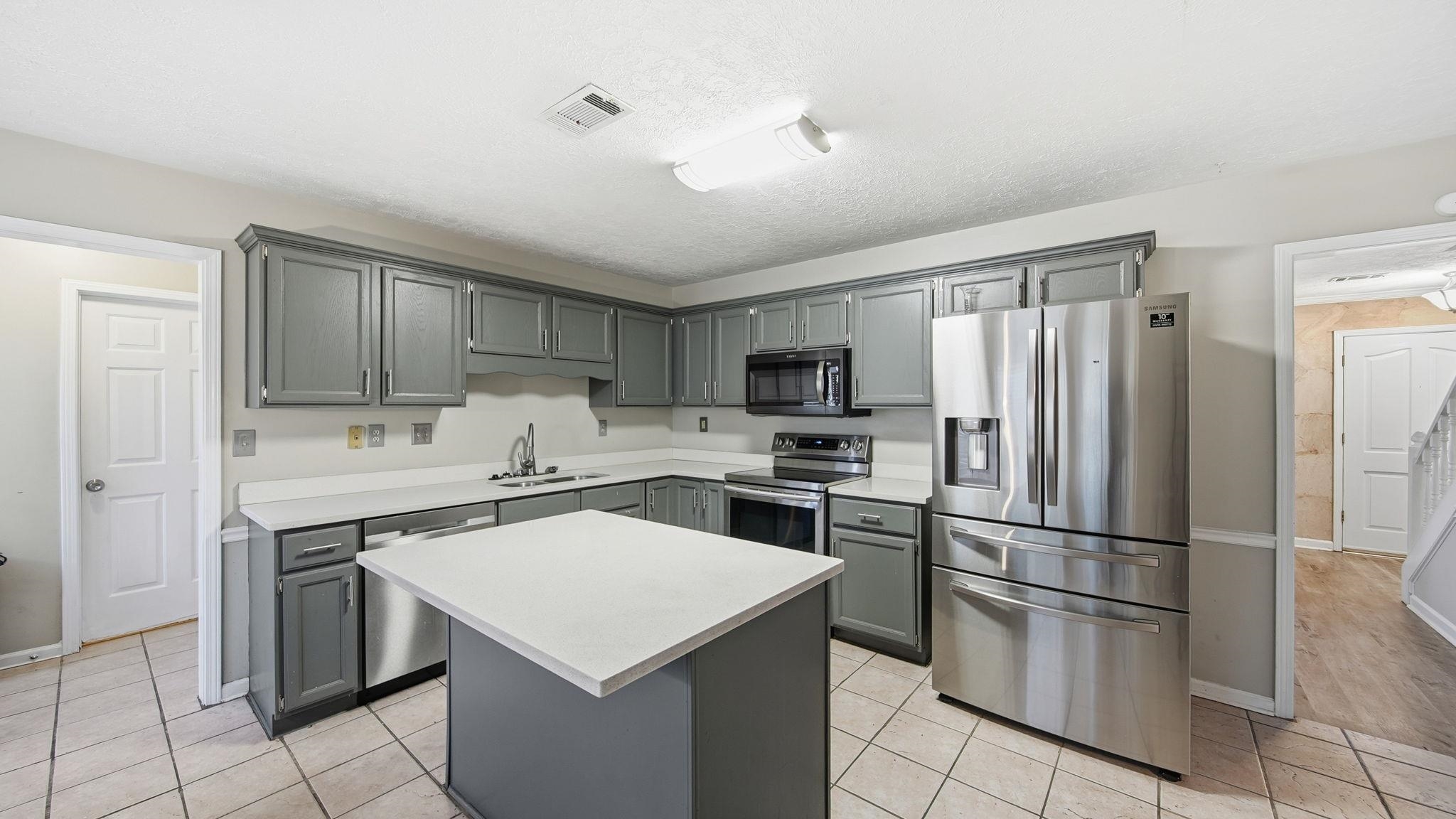 1785 Candle Ridge Drive Cordova, TN 38016 - Photo 19 of 39 Kitchen with stainless steel appliances, gray cabinets, light countertops, a center island, and a textured ceiling
