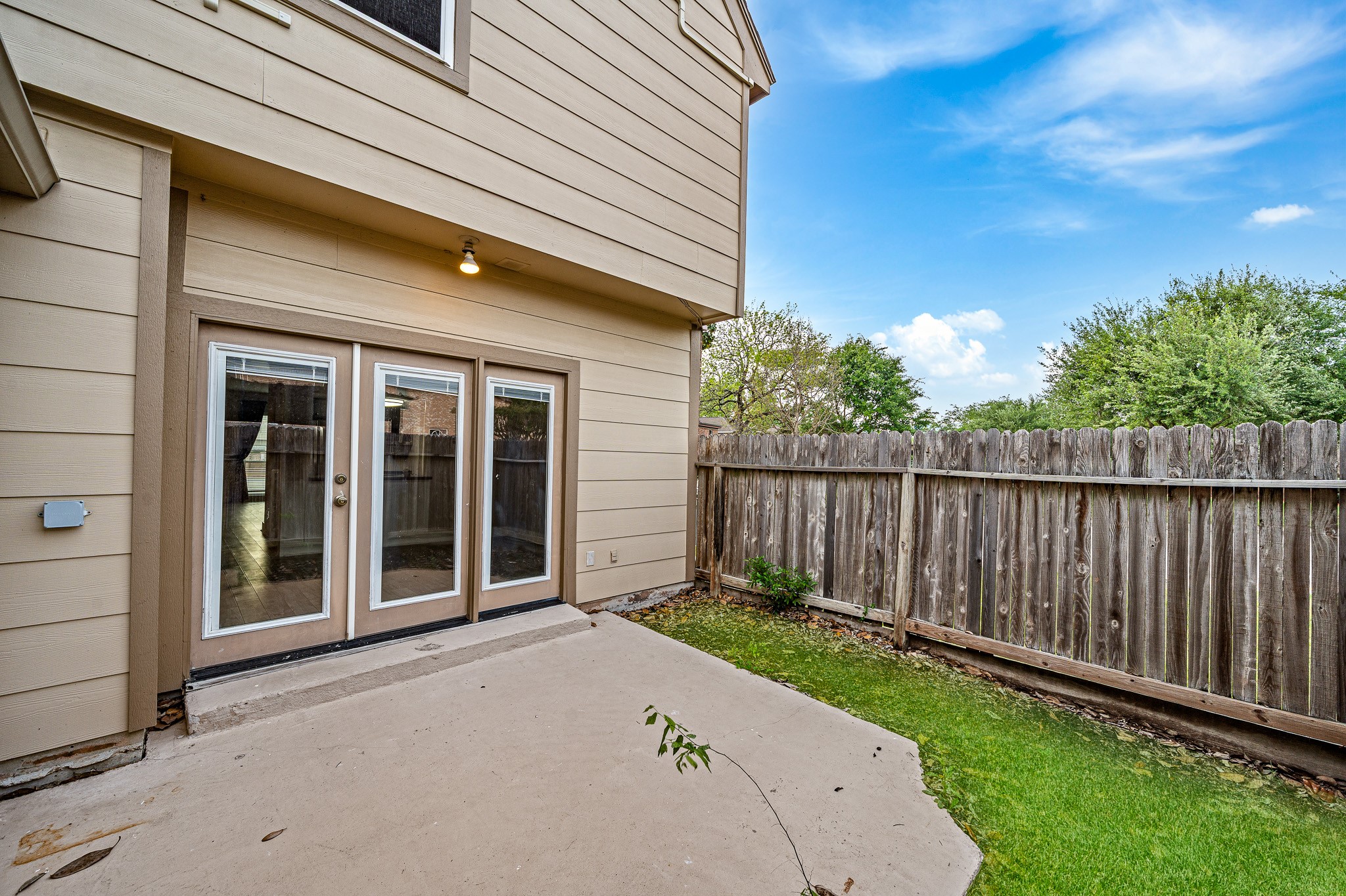830 Threadneedle Street, Unit 240 Houston, TX 77079 - Photo 26 of 33 This photo showcases a cozy backyard with a small patio area, featuring double glass doors leading into the house. The yard is enclosed by a wooden fence, providing privacy, and is accented by a bit of greenery, perfect for relaxing or small gatherings.