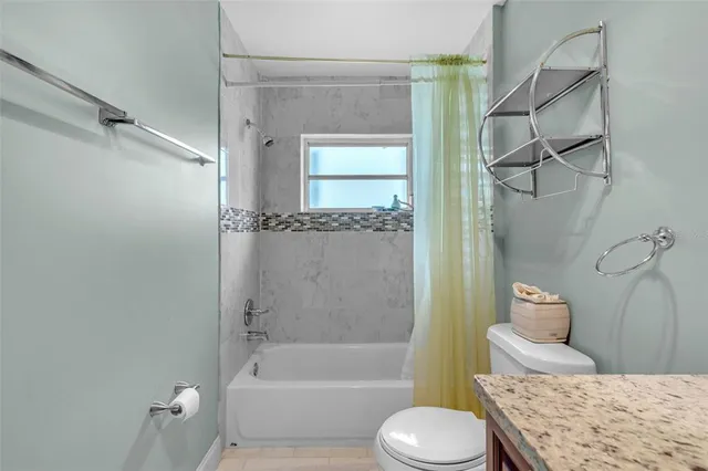 a bathroom with a granite countertop bathtub shower sink vanity and toilet