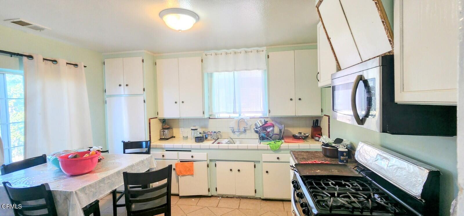 214 Smith Street Oxnard, CA 93033 - Photo 4 of 8 a kitchen with stainless steel appliances a stove a sink cabinets and a dining table