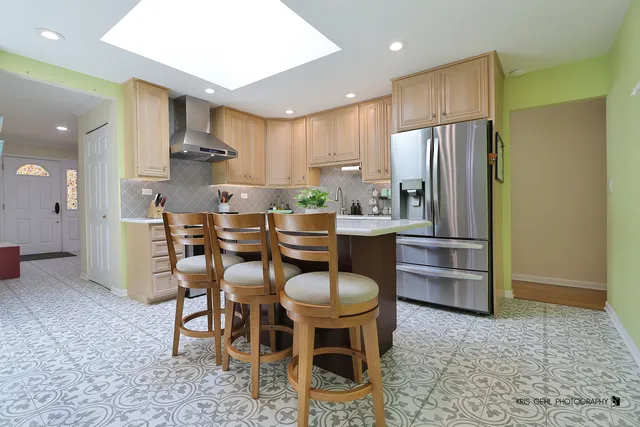 a kitchen with stainless steel appliances kitchen island granite countertop a dining table chairs and a refrigerator