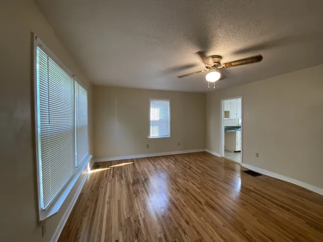 an empty room with wooden floor chandelier fan and windows