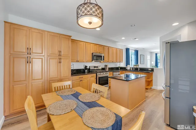 a kitchen with stainless steel appliances granite countertop a refrigerator a sink dishwasher a stove a dining table and chairs with wooden floor