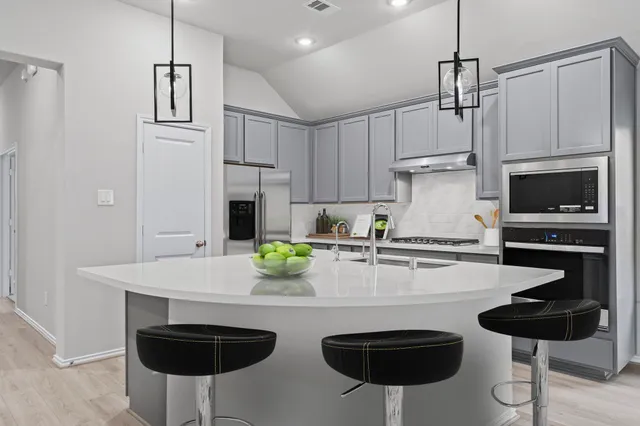 a kitchen with stainless steel appliances granite countertop a sink a stove a refrigerator and chairs with wooden floor