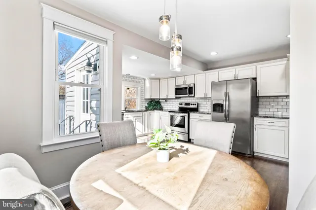 a kitchen with stainless steel appliances kitchen island granite countertop a refrigerator a stove a dining table and chairs with wooden floor