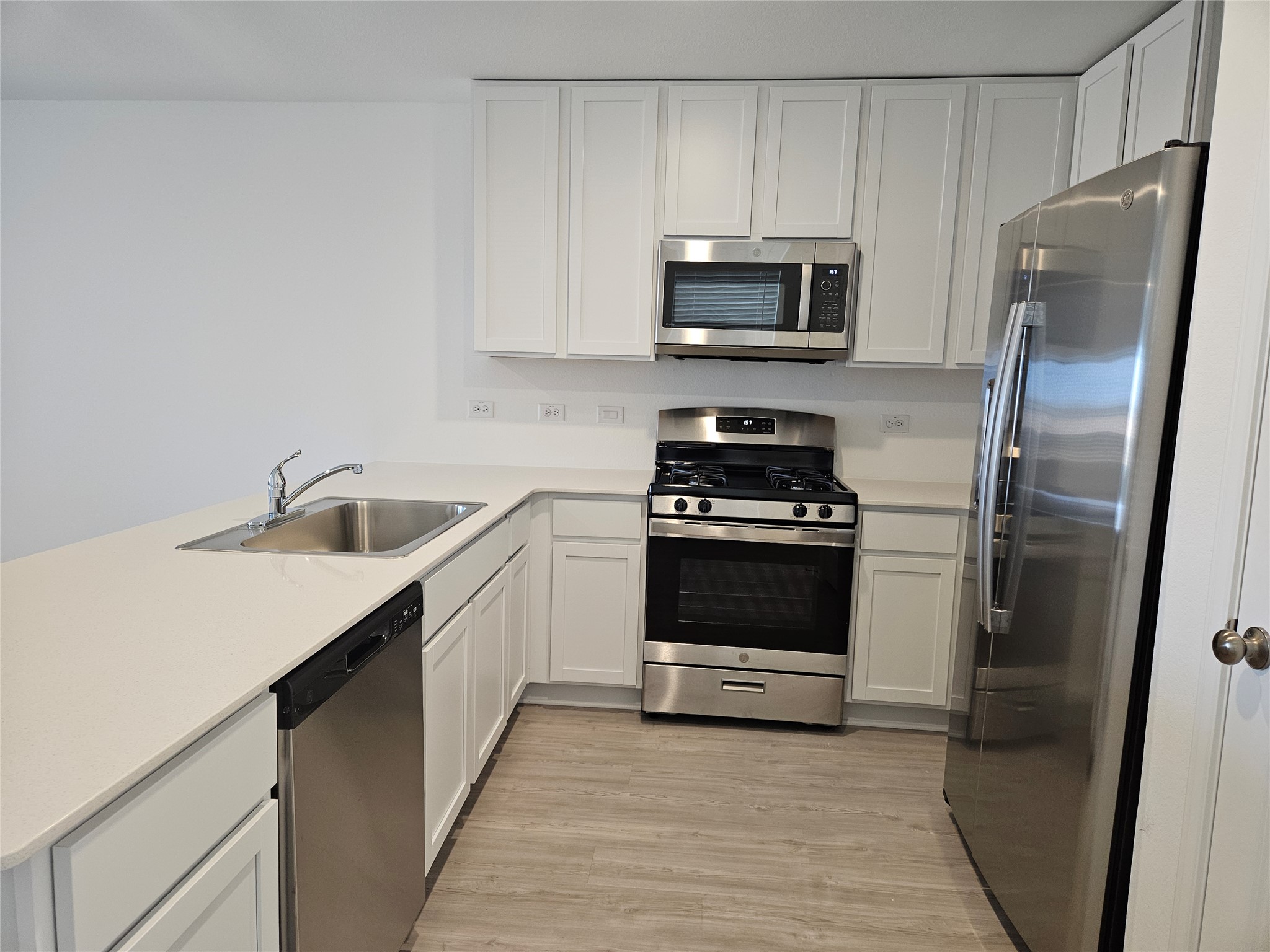 Kitchen featuring a sink, stainless steel appliances, light wood-style floors, white cabinets, and light countertops