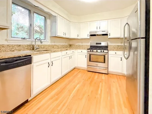 a kitchen with stainless steel appliances a stove a sink and white cabinets with wooden floor