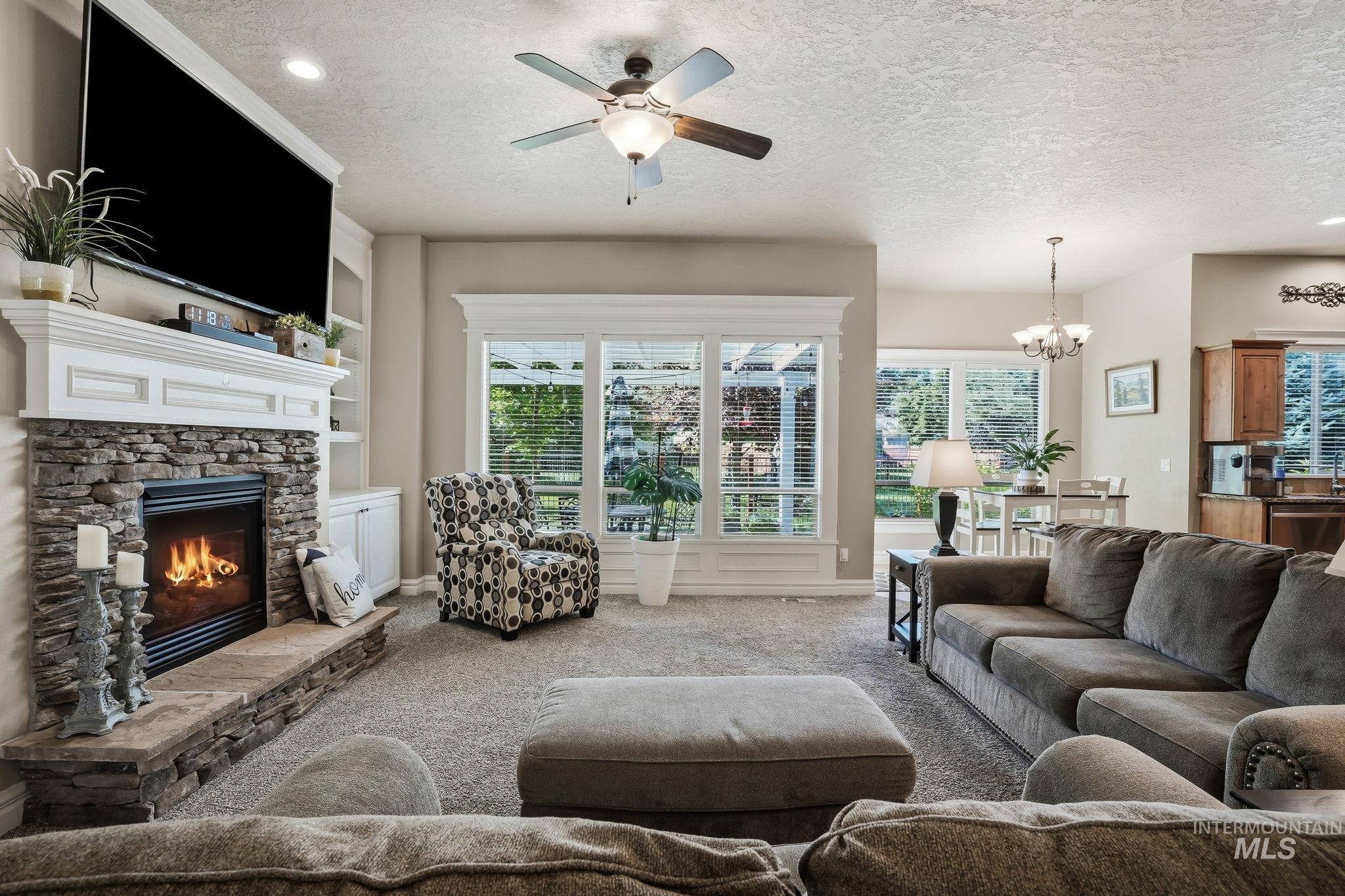 3969 North Hollymount Way Meridian, ID 83646 - Photo 6 of 47 Living area with a stone-clad fireplace and white mantel, built-in shelving, large windows with white trim, and a ceiling fan with integrated lighting