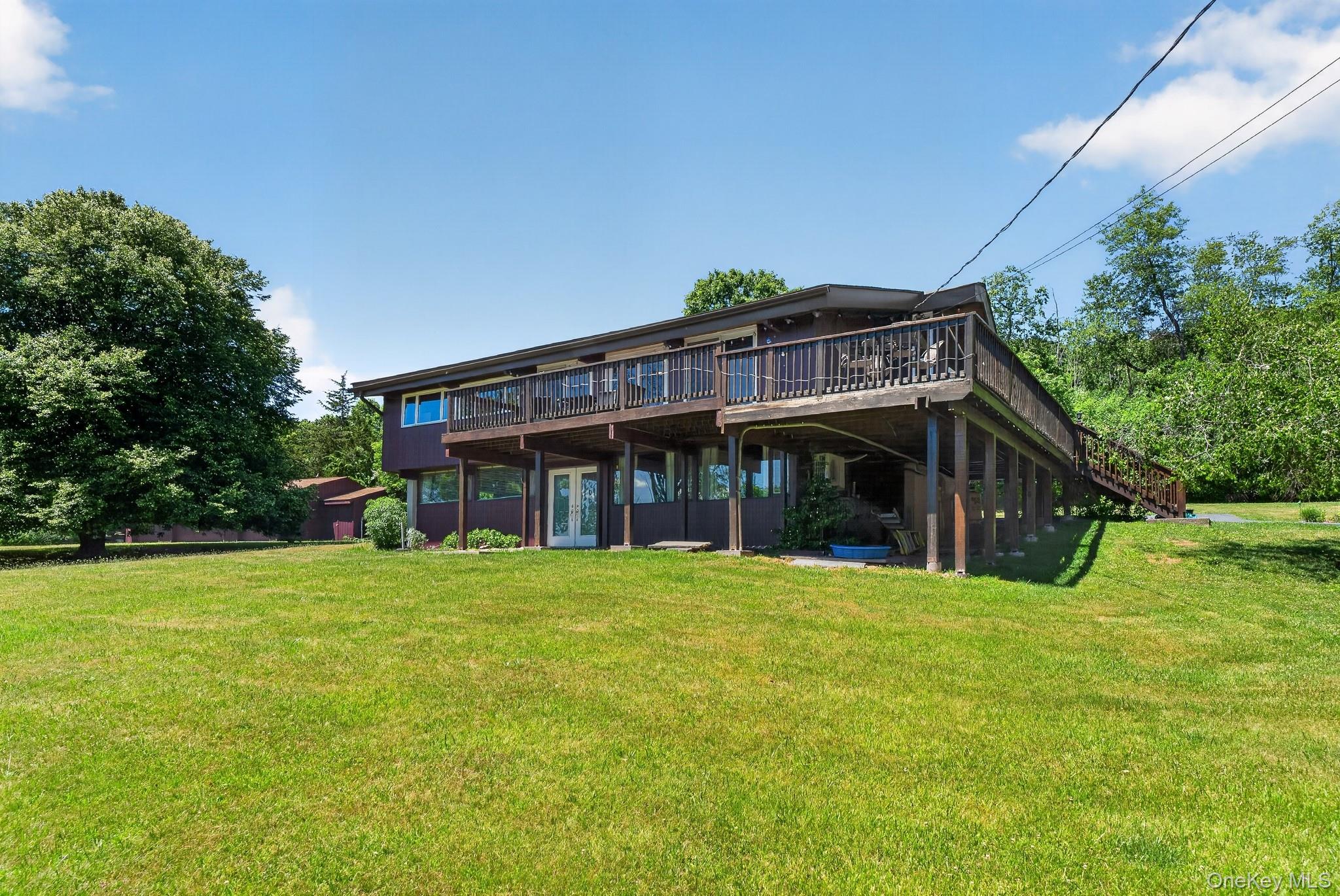 424 Laroe Road Chester, NY 10918 - Photo 20 of 43 Split-level home featuring an elevated wooden deck spanning the facade, a ground-level patio with double French doors, and an expansive grassy lawn