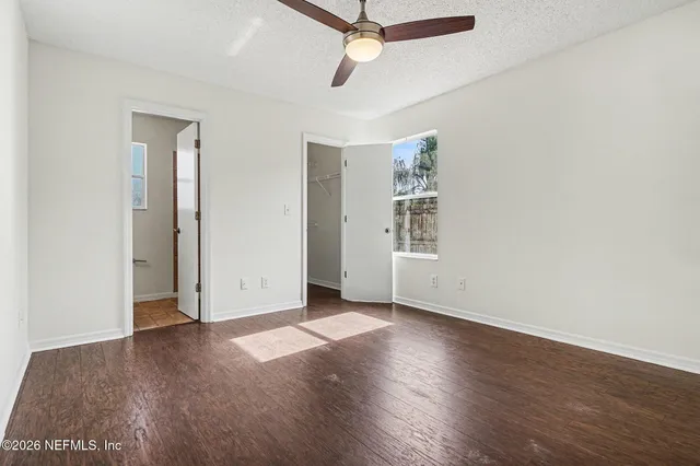 an empty room with wooden floor ceiling fan and windows