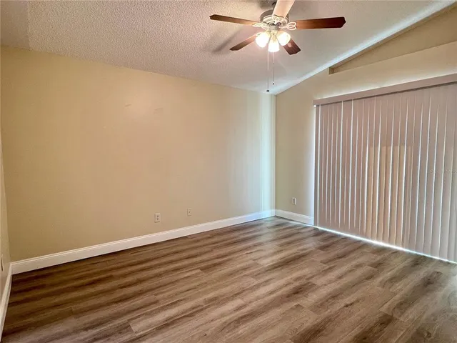 a view of an empty room with wooden floor and a ceiling fan