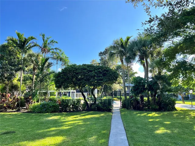 a view of a fountain in front of a house with a big yard and large trees